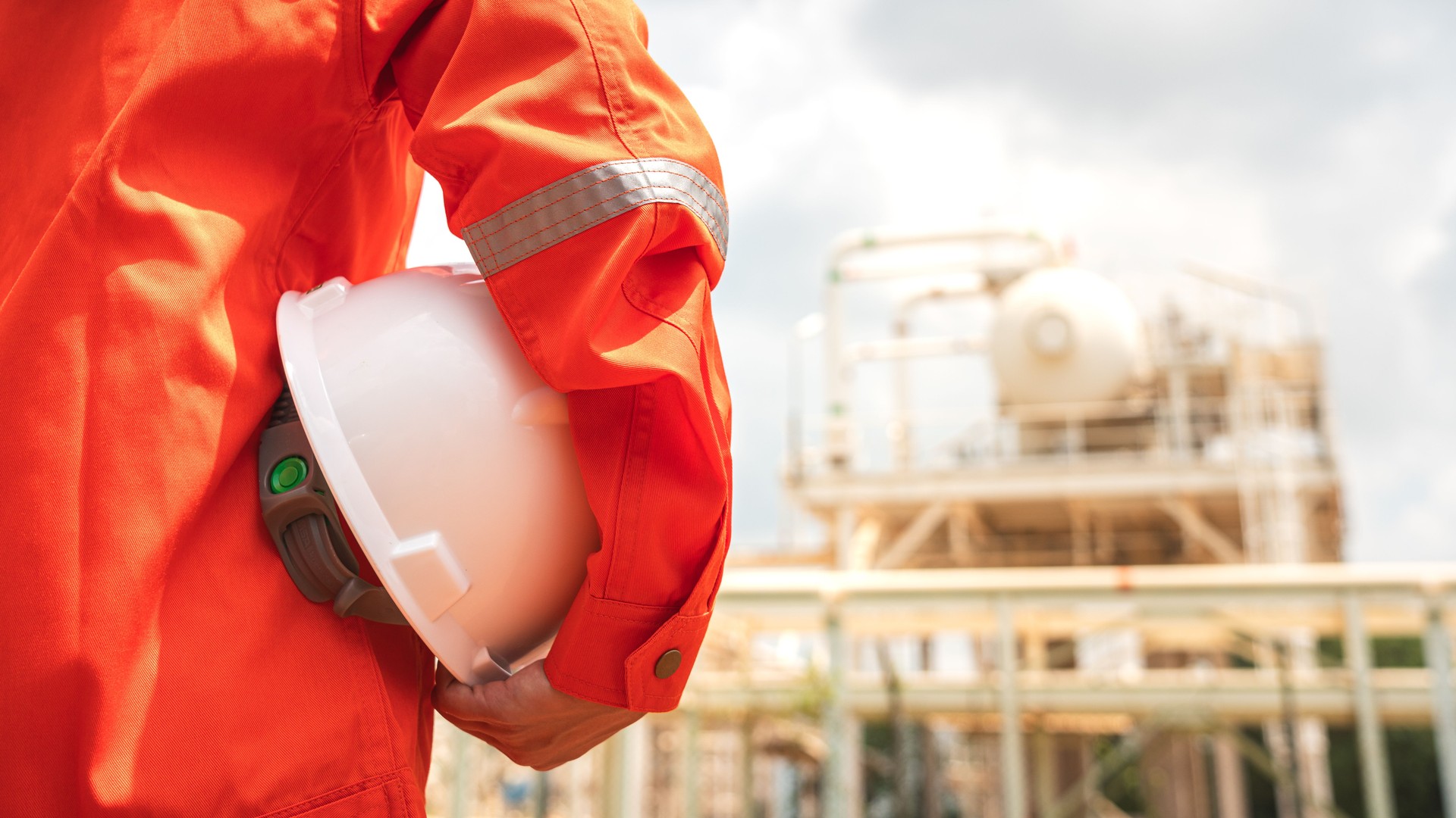 Engineer holding safety helmet with refinery plant.